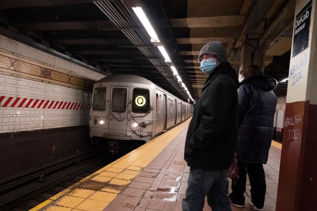 Commuters wearing masks wait for a train that is coming into the station